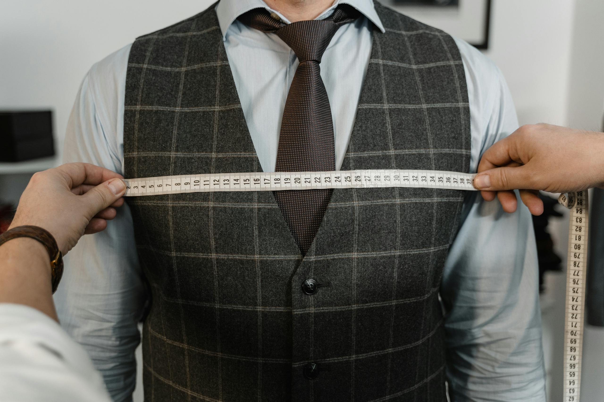 A tailor measuring a client's chest for a bespoke suit in a professional setting.