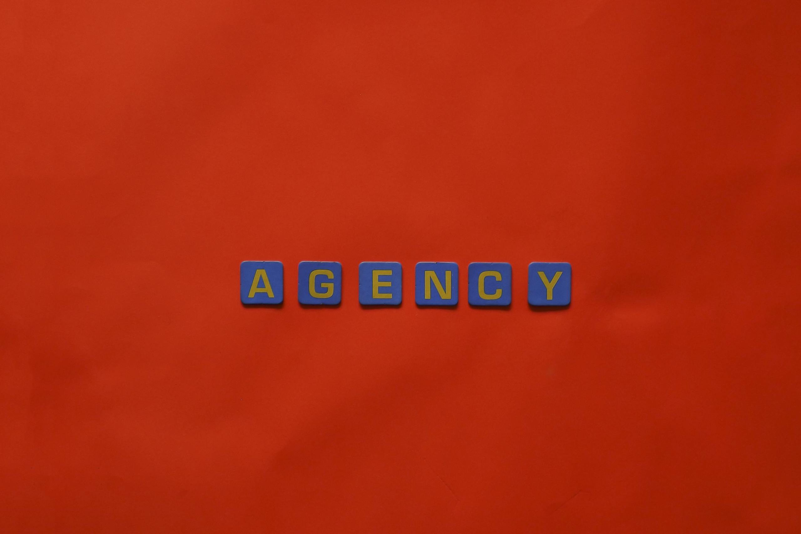 Blue letter tiles spelling 'AGENCY' on a vibrant red background, ideal for creative promotion.